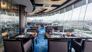 Een restaurant met gedekte tafels, grote ramen met uitzicht over de stad en een modern plafondontwerp.