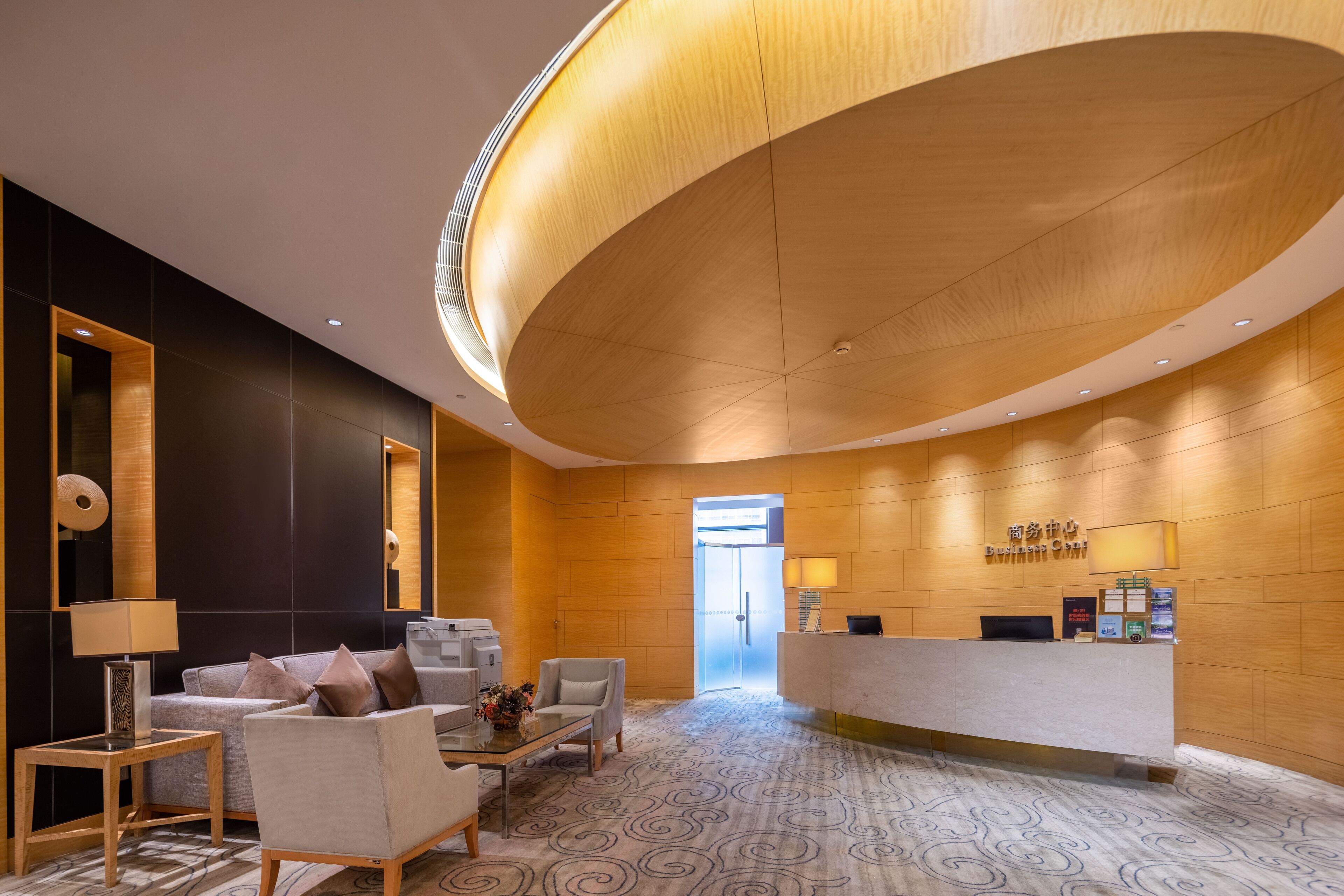 Een modern ingerichte receptie met een gebogen houten plafond, een receptiebalie en een zithoek met een bank en stoelen.