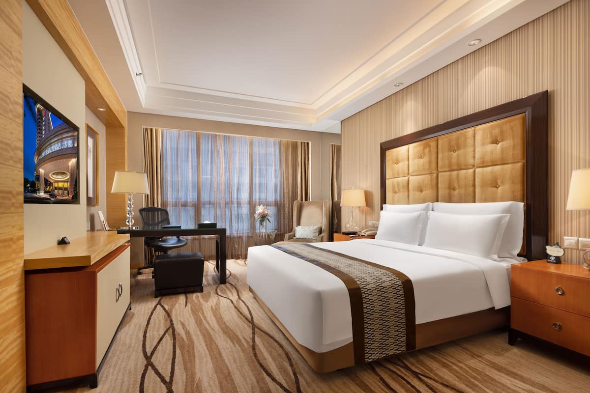 A hotel room with a large bed, a desk, a chair, and a view of the cityscape.