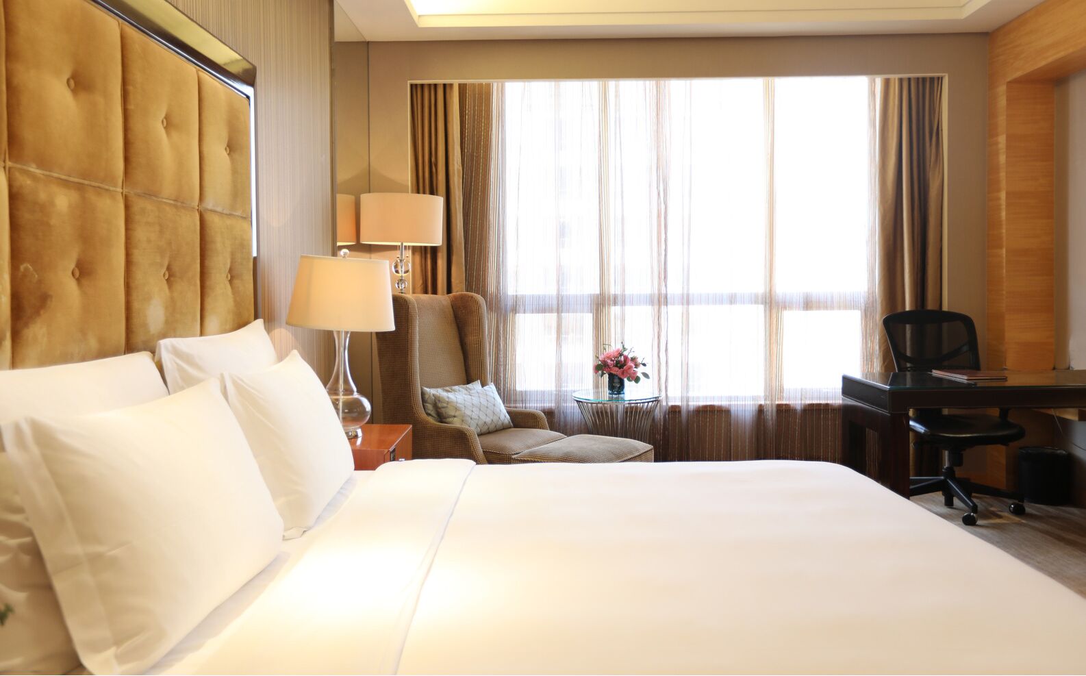 A hotel room with a large bed, a desk, a chair, and a window with curtains.