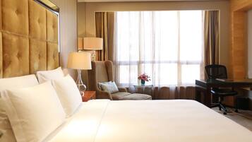 A hotel room with a large bed, a desk, a chair, and a window with curtains.