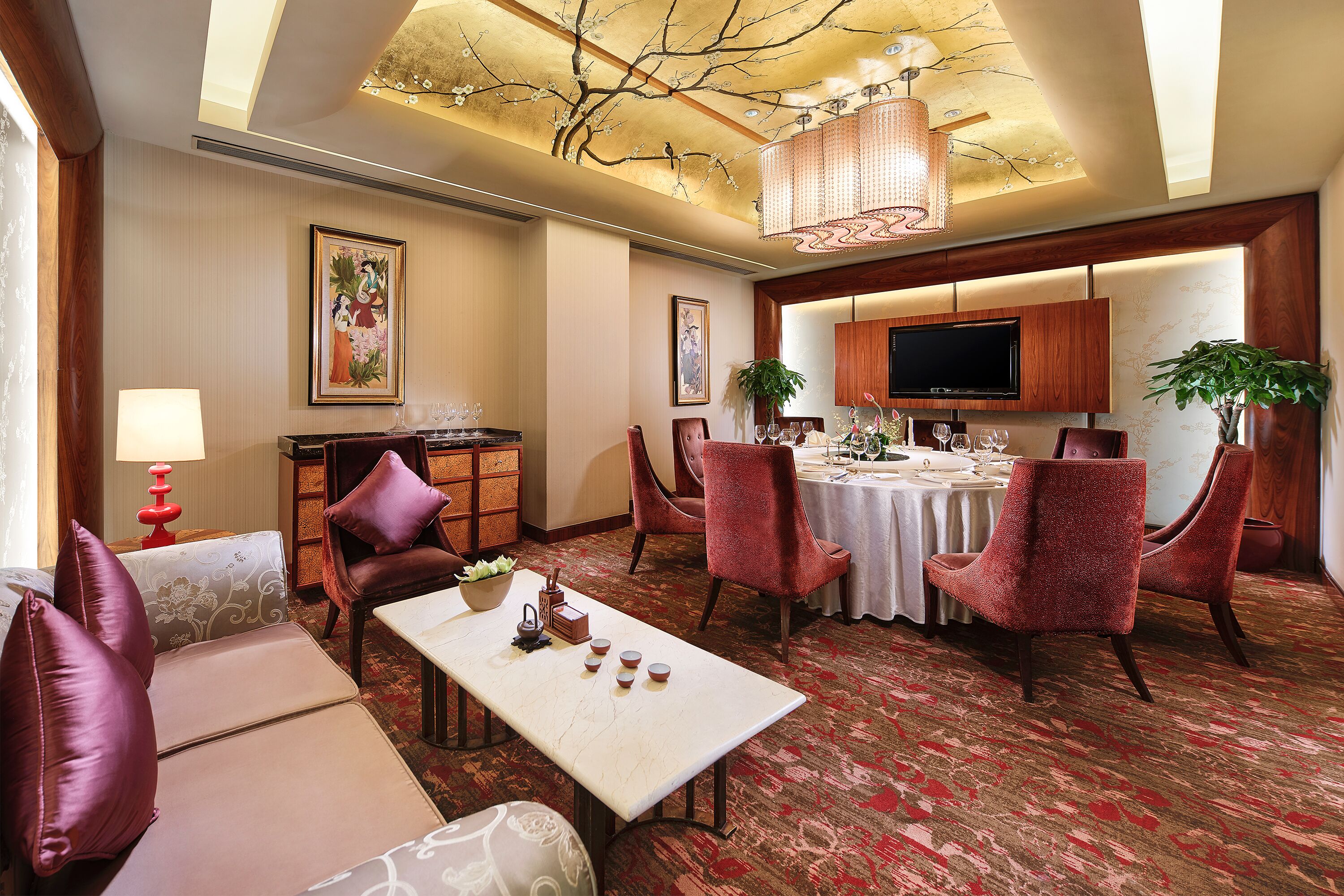 A hotel room with a dining area, a sofa set, a television, and a chandelier.
