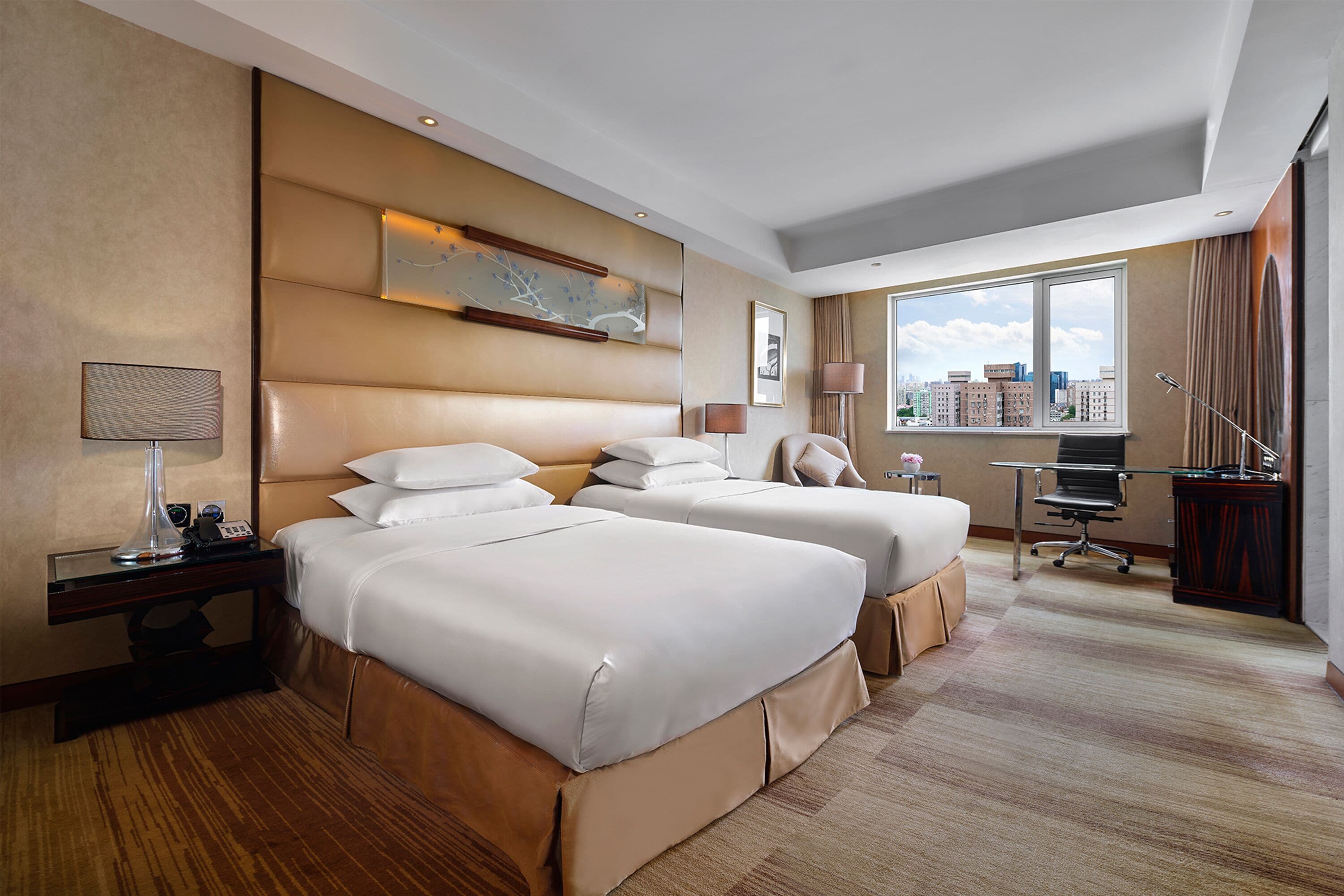 Une chambre d’hôtel avec deux lits, un bureau, une chaise et une grande fenêtre donnant sur la ville.