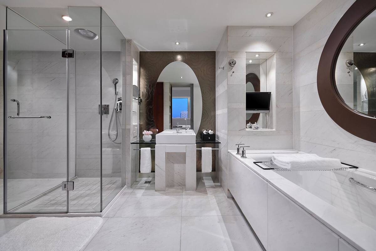 A modern bathroom with a glass shower enclosure, a vanity with a large mirror, and a bathtub.