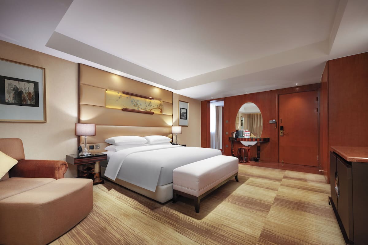 A hotel room with a large bed, a desk, a chair, a mirror, and a wardrobe.