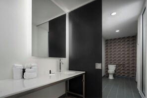 A modern bathroom with a white sink, large mirror, and dark patterned wall. - Aloft by Marriott Richmond West Short Pump (Richmond)