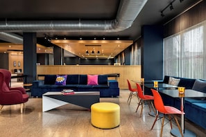 A modern lounge area with a sofa, red chair, yellow ottoman, and a dining table with red chairs.
