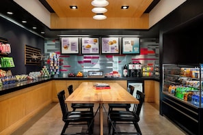 A modern cafe with a wooden table, black chairs, a menu board, and a beverage cooler.