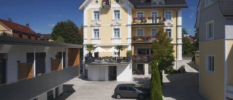 A multi-story building with balconies, a covered outdoor seating area, and a parking lot.