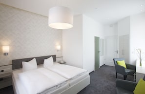 Ein modernes Hotelzimmer mit einem großen Bett, Nachttischen, einem Schreibtisch und einem Sessel.
