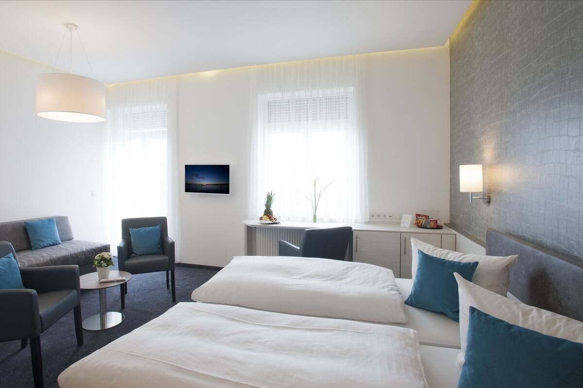 Ein Hotelzimmer mit einem Bett, einem Sofa, einem Sessel, einem kleinen Tisch und einem Fernseher.