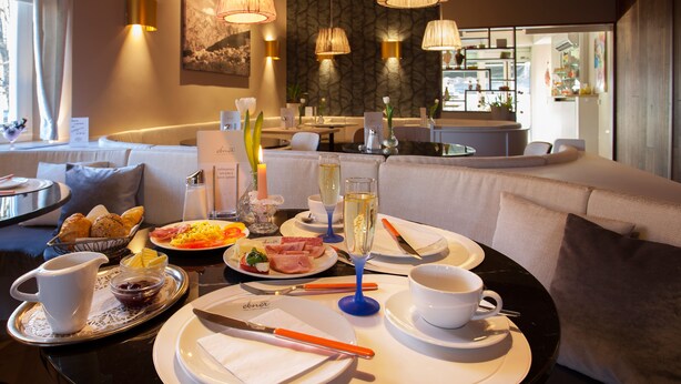 Un coin repas avec une table ronde mise pour le petit-déjeuner, comprenant des assiettes, des couverts et un verre de champagne.