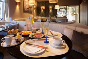 A dining area with a round table set for breakfast, including plates, cutlery, and a glass of champagne. - Hotel Café Ebner (Lindau)