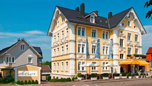 Un grand bâtiment jaune, orné de plusieurs drapeaux, avec une enseigne indiquant « ebner hotel & cafe », et des tables à l’extérieur, protégées par des parasols.