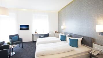Quarto de hotel com duas camas, uma escrivaninha, uma cadeira e uma televisão.