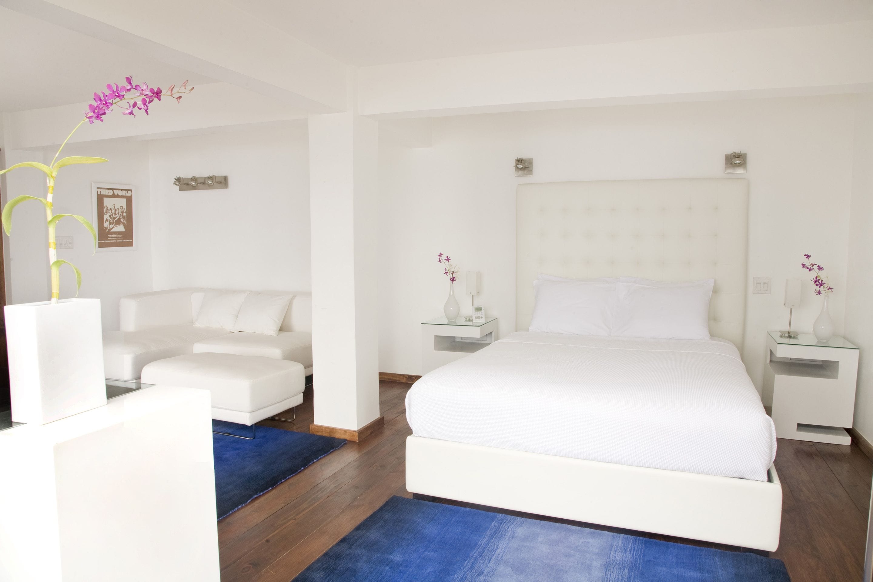 A modern bedroom with a large bed, a white sofa, and a small table with a vase.