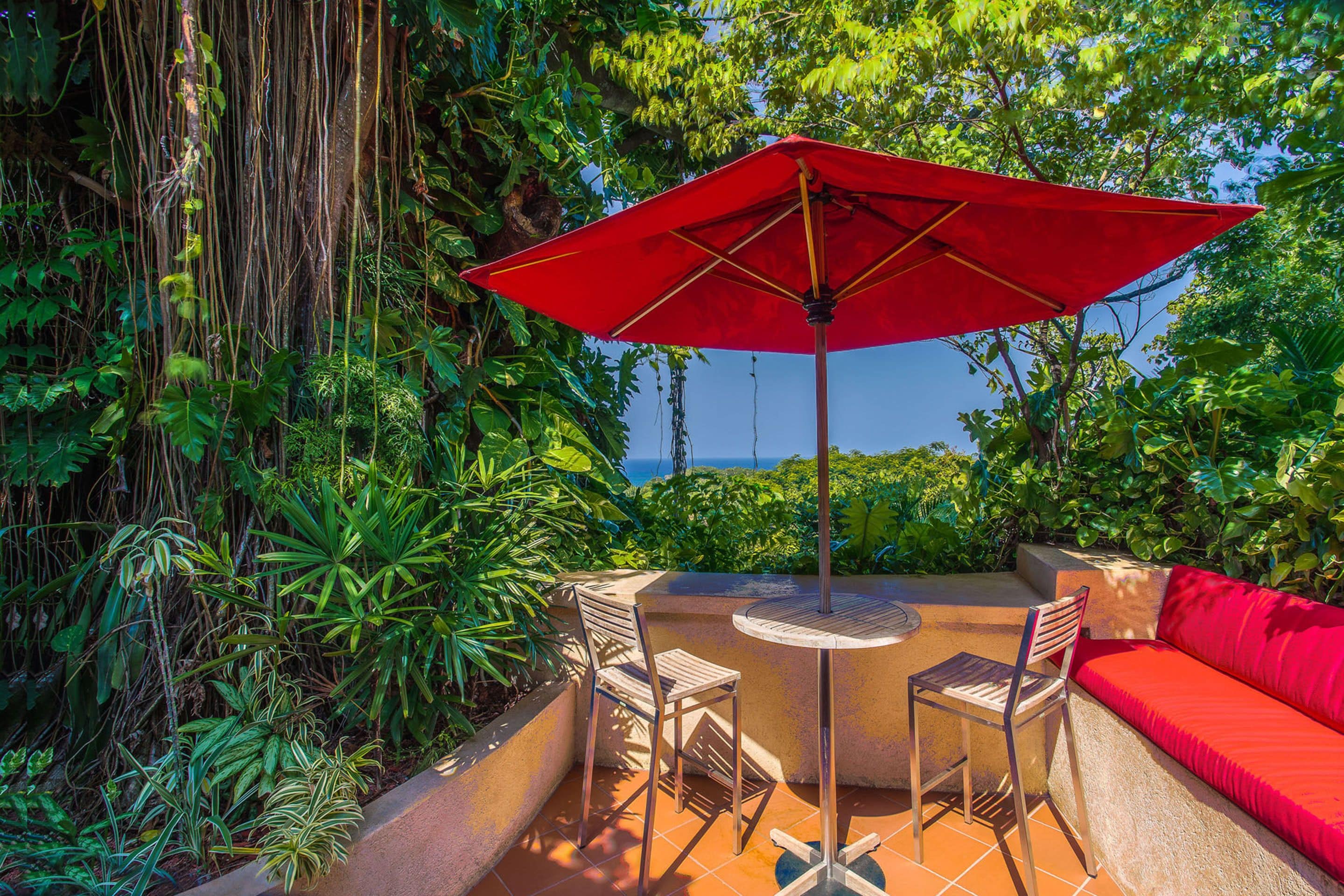 An outdoor patio with a red umbrella, a round table, and a red sofa.