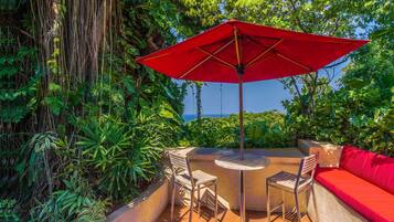 An outdoor patio with a red umbrella, a round table, and a red sofa.