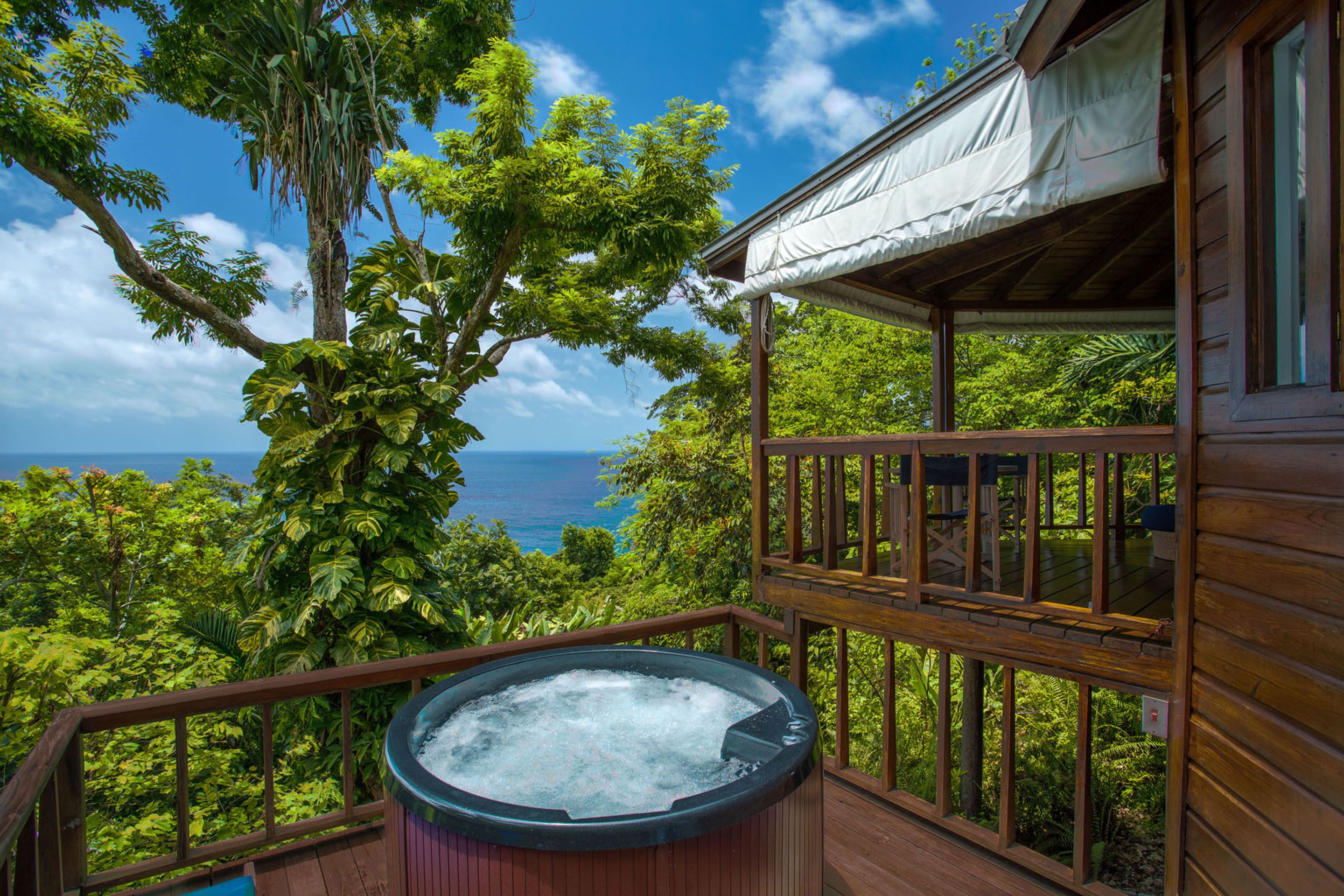 A wooden deck with a hot tub, overlooking lush greenery and the ocean.