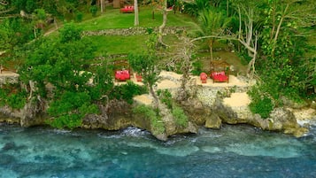 Um resort costeiro com várias cabanas vermelhas numa formação rochosa, com vista para águas azul-claras.