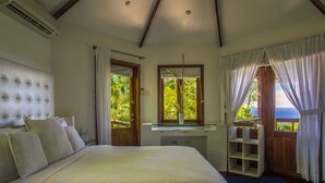 A bedroom with a large bed, a vanity with a mirror, and a view of the outdoors.