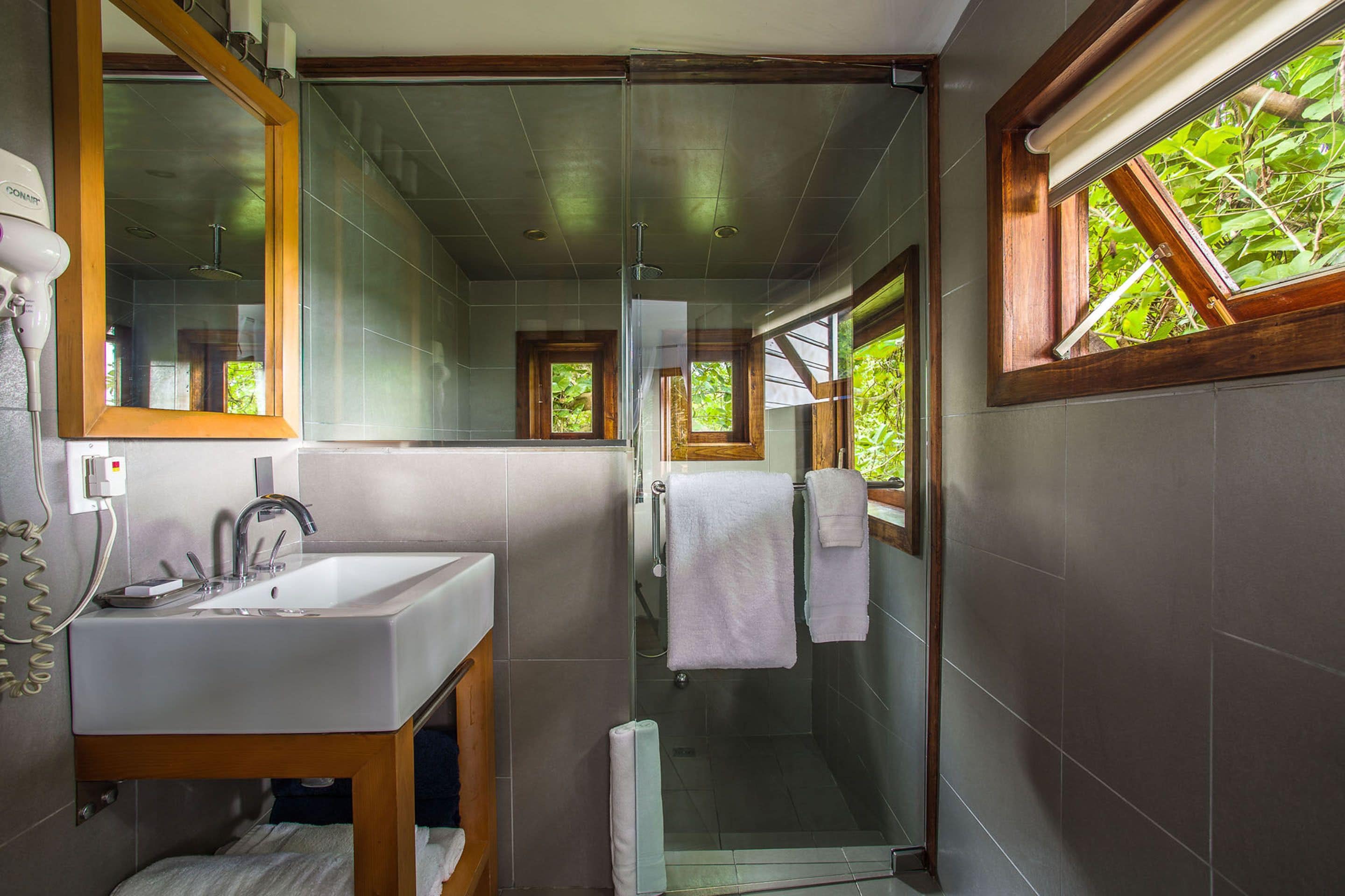 A modern bathroom with a glass-enclosed shower, a sink with a mirror, and a window providing natural light.