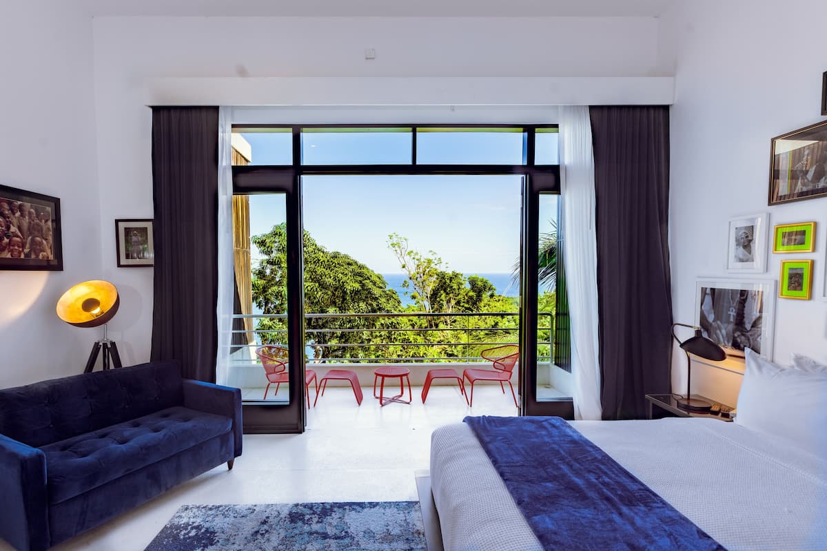 Une chambre moderne avec un grand lit, un canapé bleu et un balcon avec des chaises rouges.