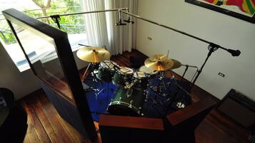 A drum set in a room with wooden flooring, a window with curtains, and a framed picture on the wall.