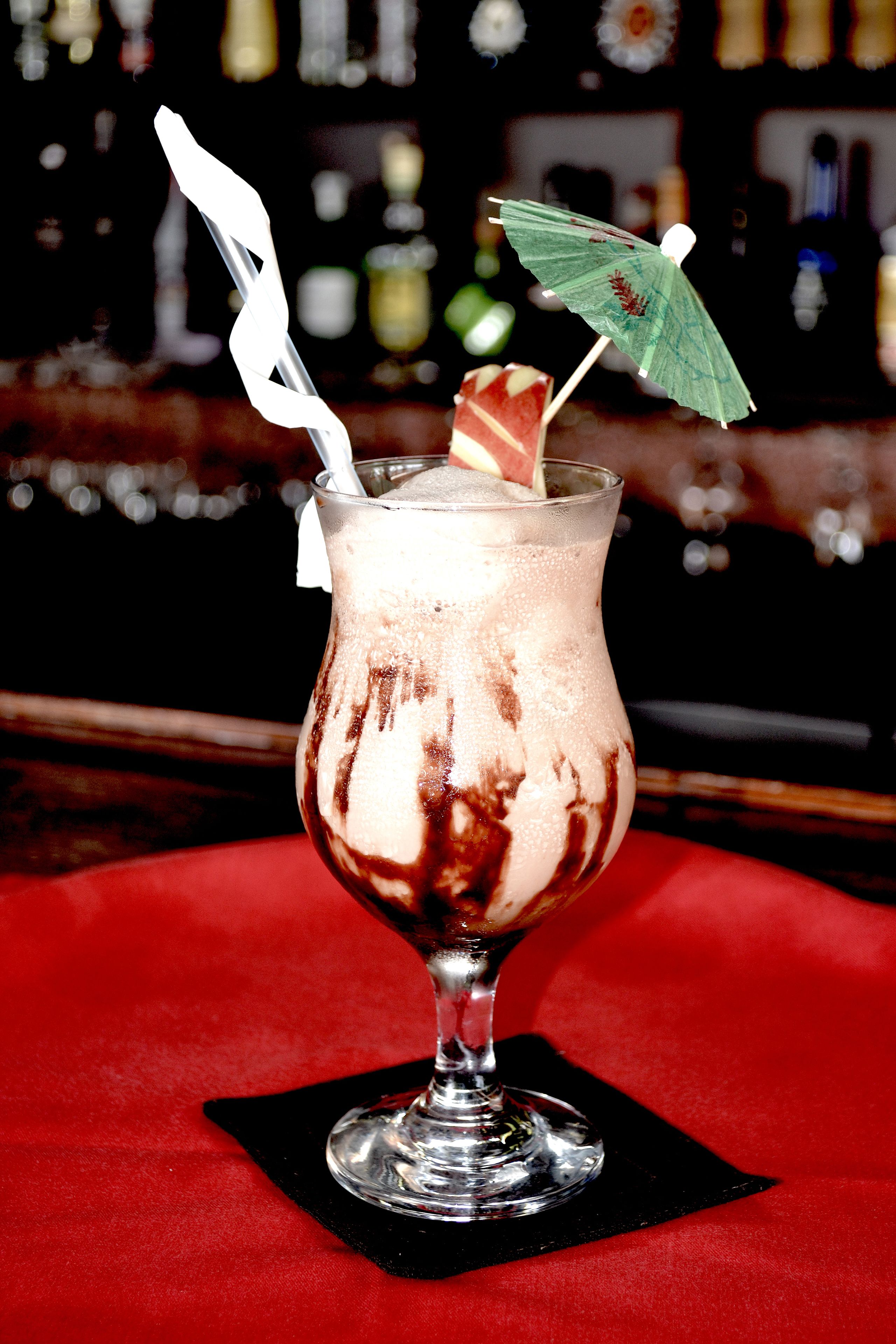 Een cocktail met een rietje en een decoratieve parasol op een rode tafelkleed.