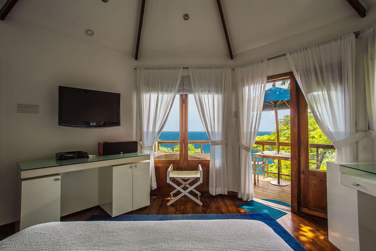 Une chambre à coucher avec un lit, un bureau, une chaise, une télévision et une vue sur l’océan.