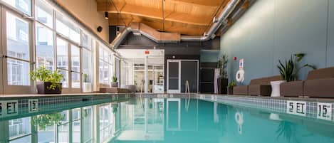 An indoor swimming pool with clear water, wooden ceiling, large windows, and potted plants.
