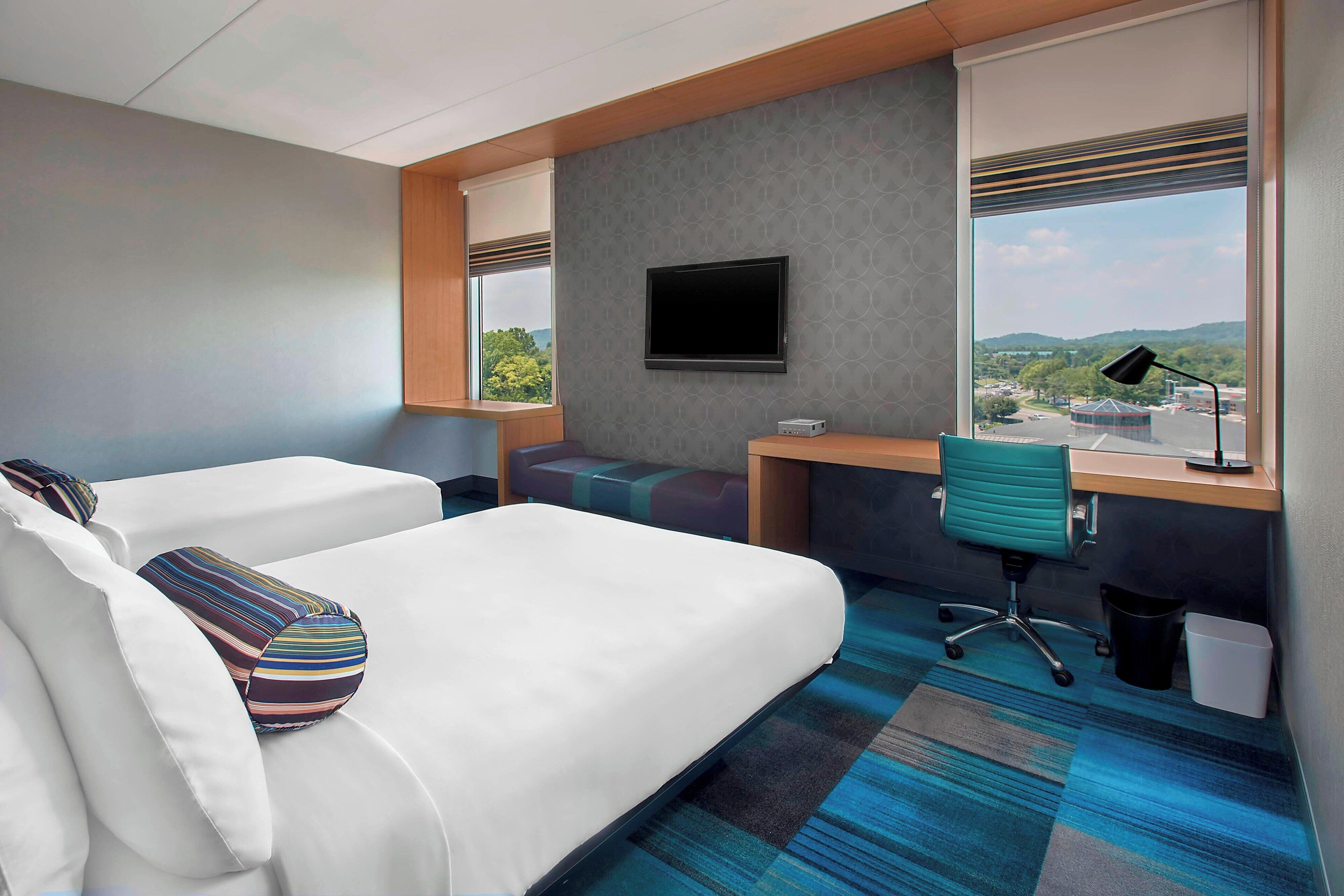 Habitación de hotel con dos camas, un escritorio, una silla, un televisor y vistas al exterior.