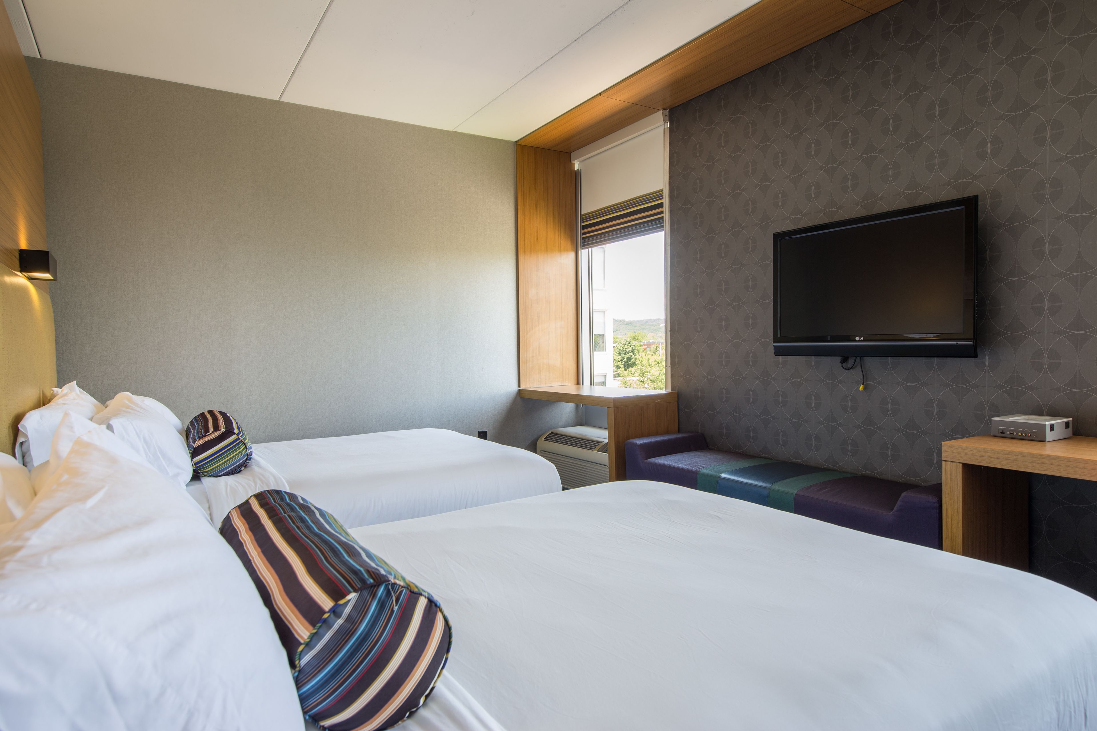 A hotel room with two beds, a TV, a desk, and a window with a view.