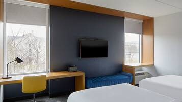 Et moderne hotelværelse med et stort vindue, et skrivebord med stol, et fladskærms-tv og to senge.