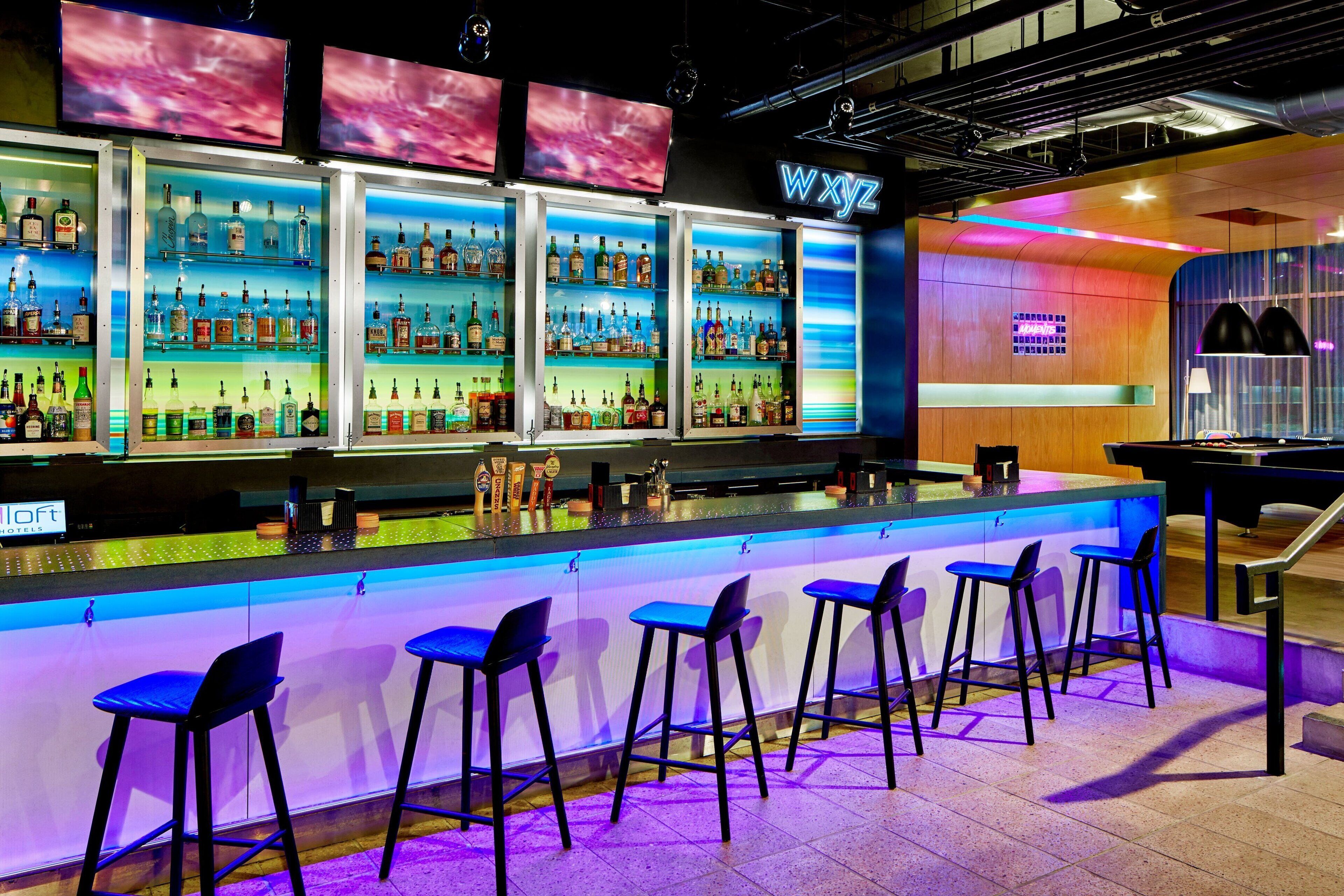 A bar area with multiple shelves of liquor bottles, bar stools, and a neon sign.