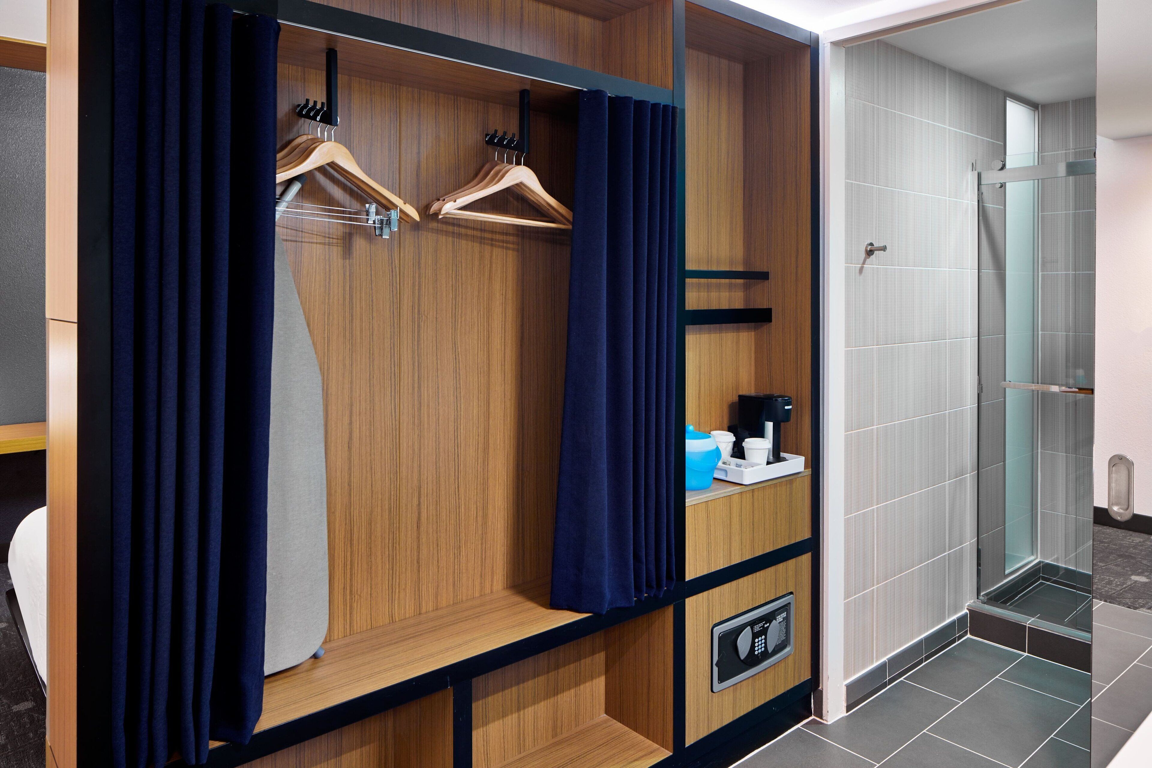 Une chambre d’hôtel avec une armoire en bois, un espace douche et une petite étagère contenant des articles de toilette.
