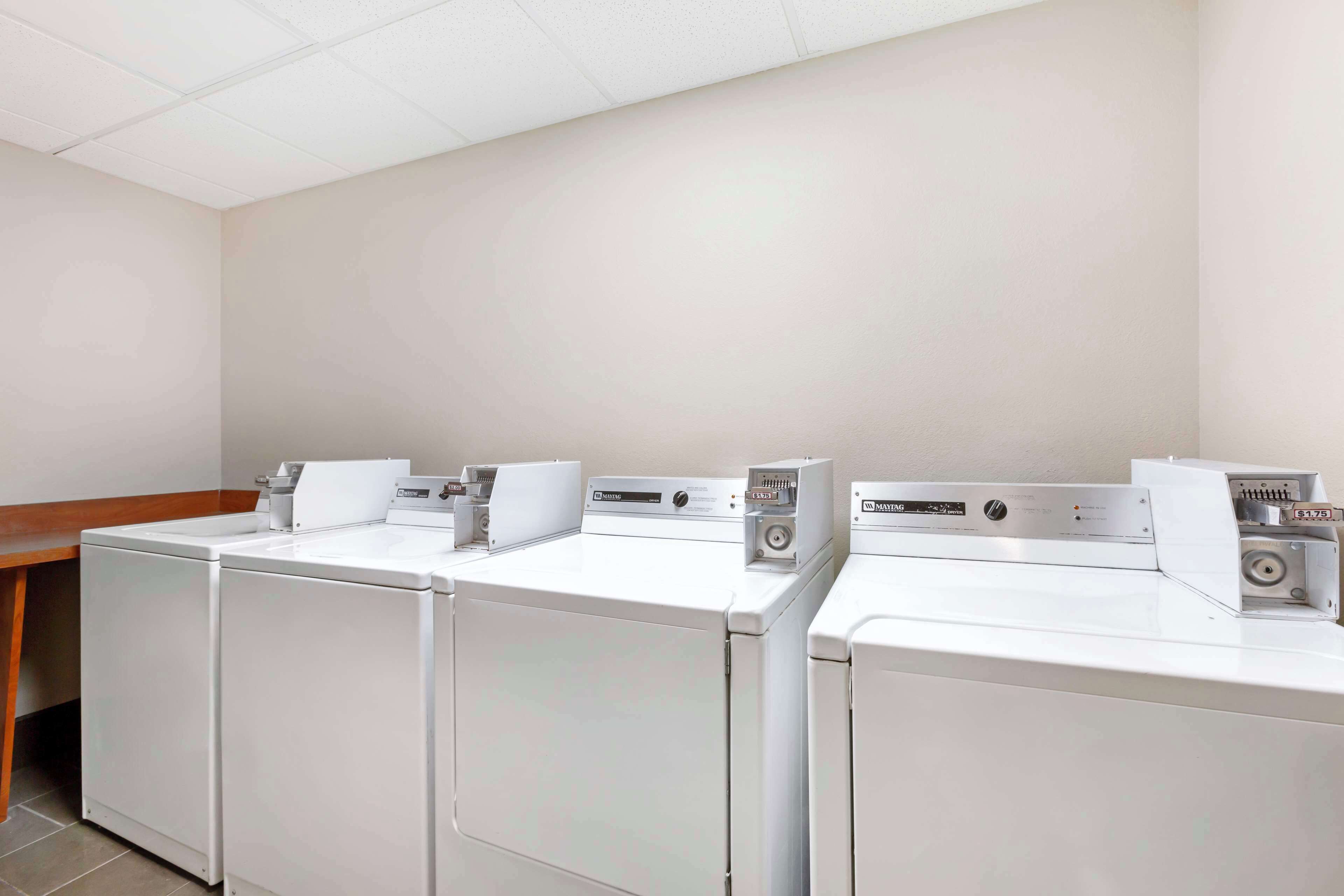 A laundry room with three front-loading washing machines and a wooden bench.