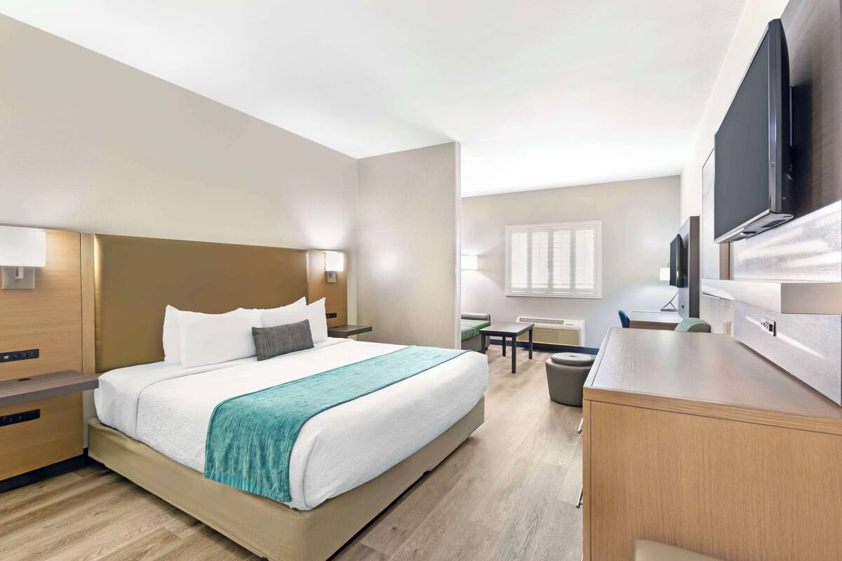 A hotel room with a bed, bedside tables, a desk, a chair, a TV, and a window.