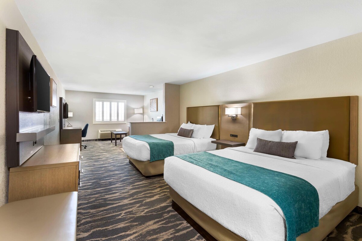 A hotel room with two beds, a desk, a TV, and a window.