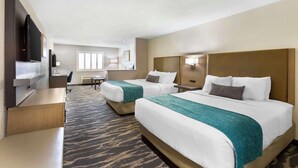 A hotel room with two beds, a desk, a TV, and a window.