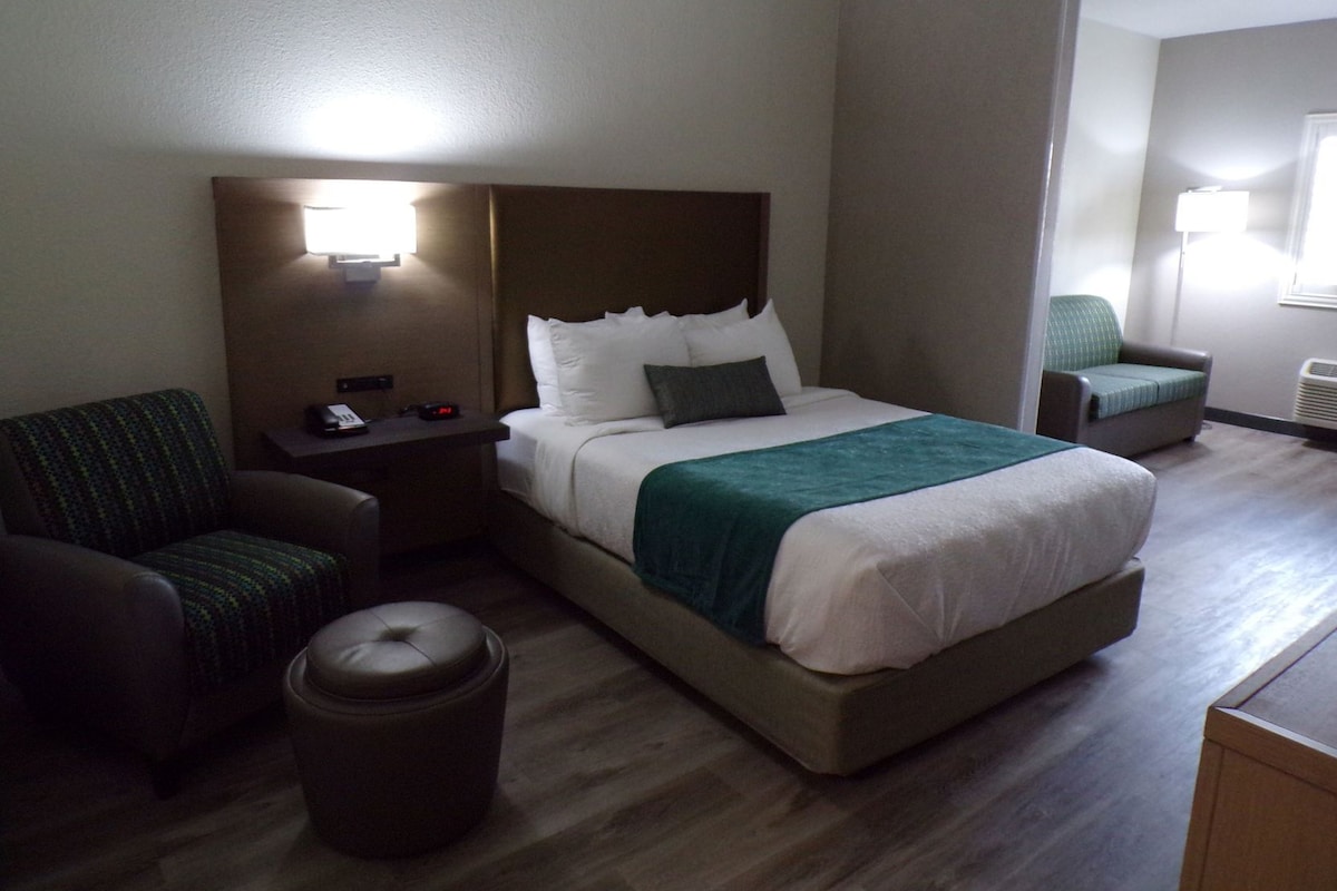 A hotel room with a bed, a desk, a chair, and a trash bin.