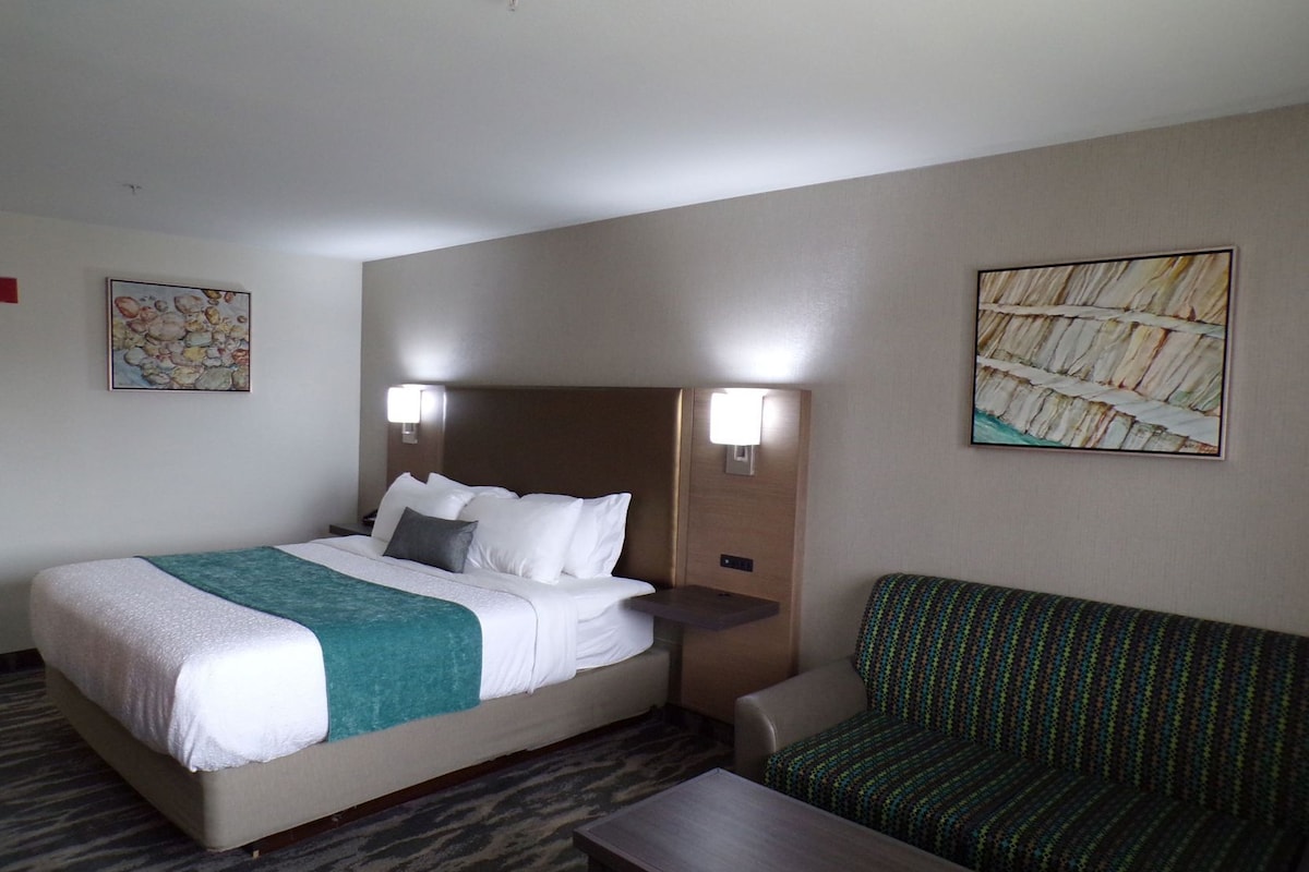 A hotel room with a bed, a green sofa, a wooden nightstand, and two wall-mounted lamps.