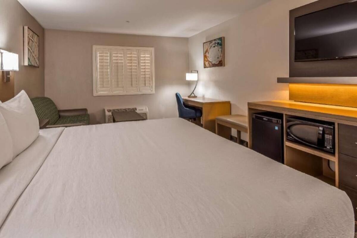 A hotel room with a large bed, a desk with a chair, a television, and a microwave.