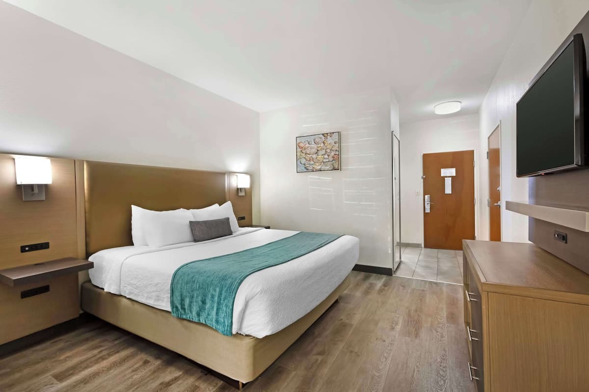 A hotel room with a bed, bedside tables, a flat-screen TV, and a wooden cabinet.