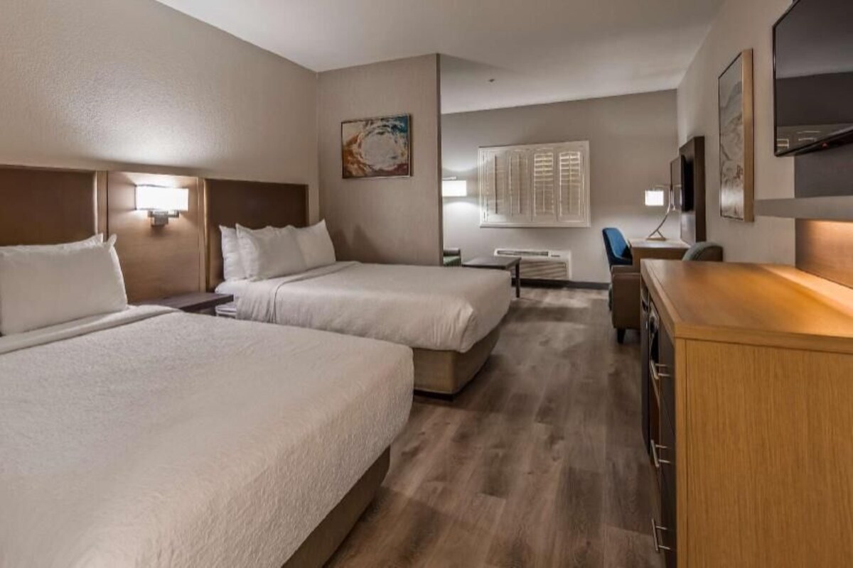 A hotel room with two beds, a desk, a chair, and a TV.