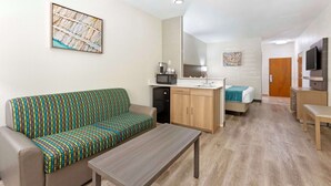 A compact hotel room with a sofa, a small table, a kitchenette, a bed, and a TV.