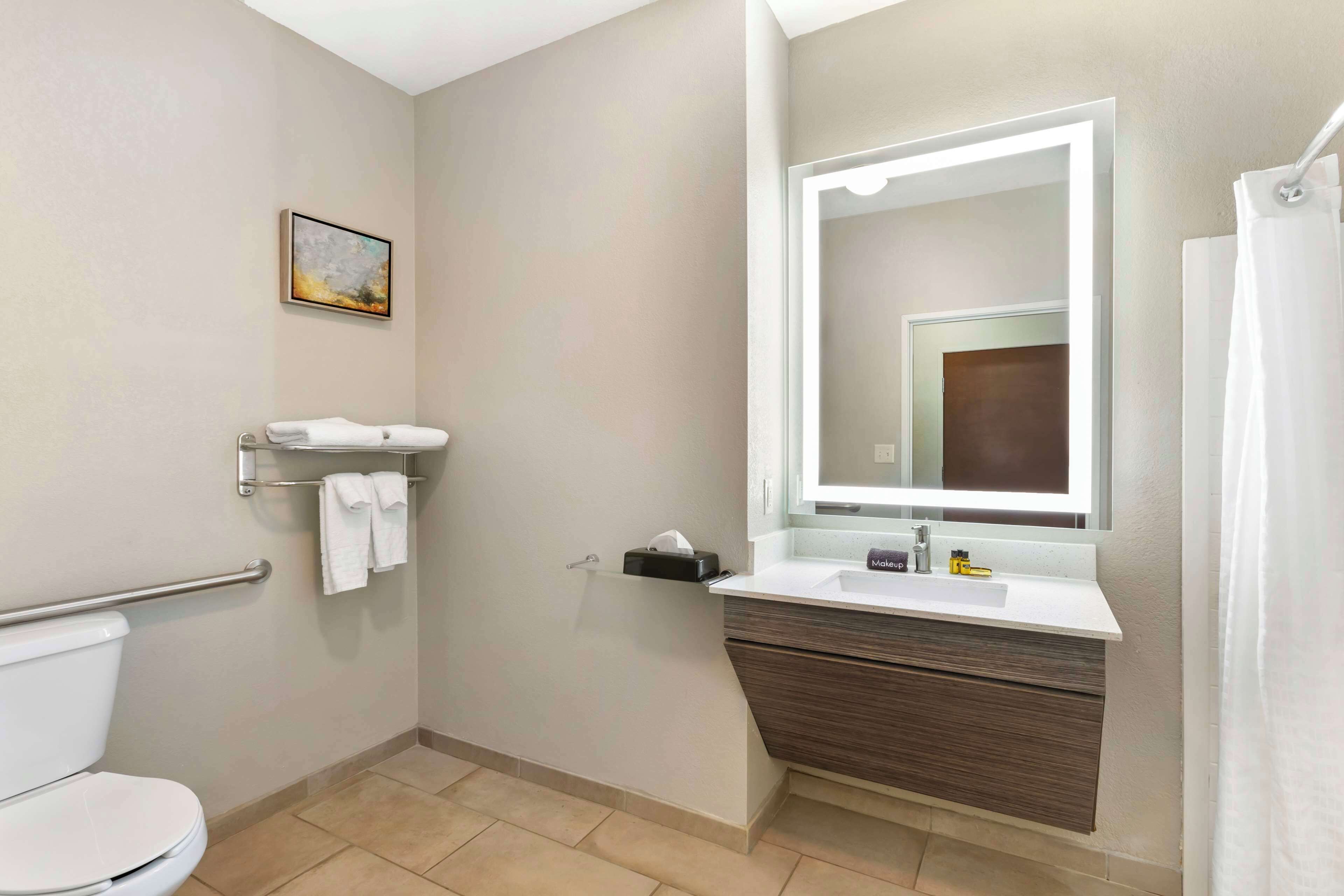 A modern bathroom with a toilet, a sink with a mirror, a towel rack, and a shower curtain.