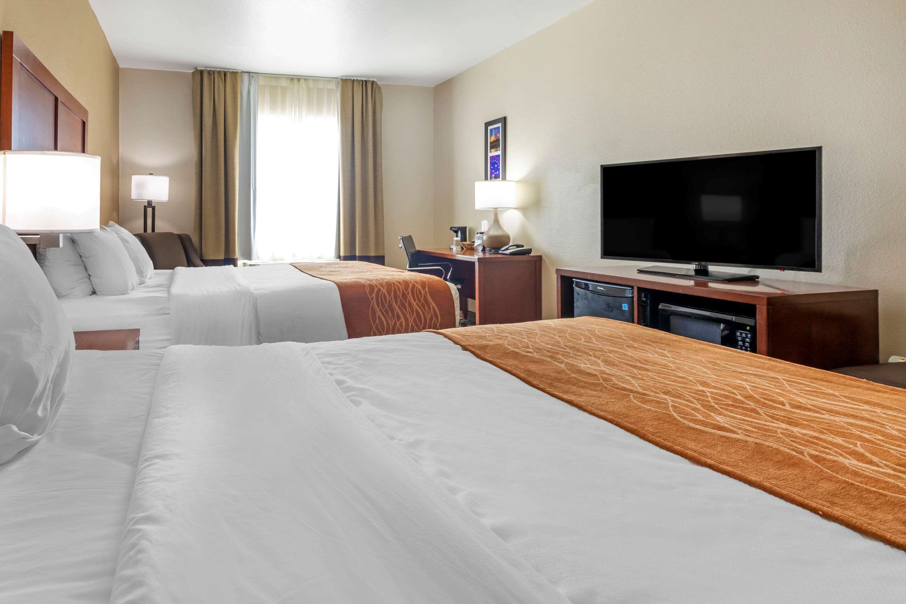 A hotel room with two beds, a television, a desk with a lamp, and a window with curtains.
