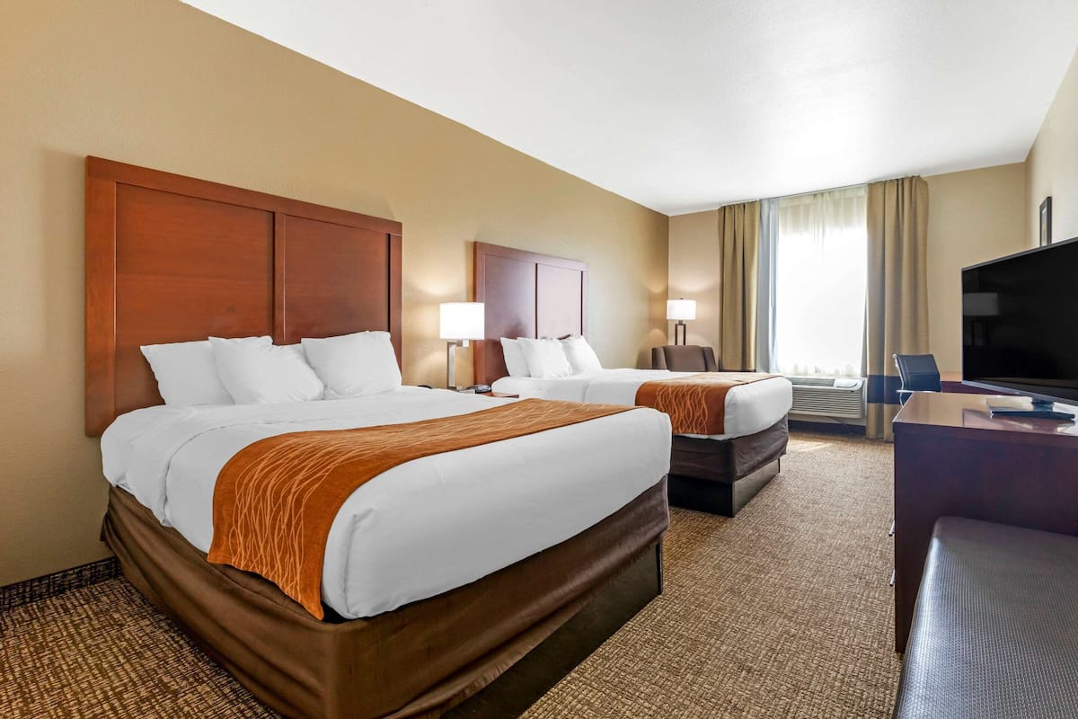 A hotel room with two beds, a desk, a television, and a window with curtains.