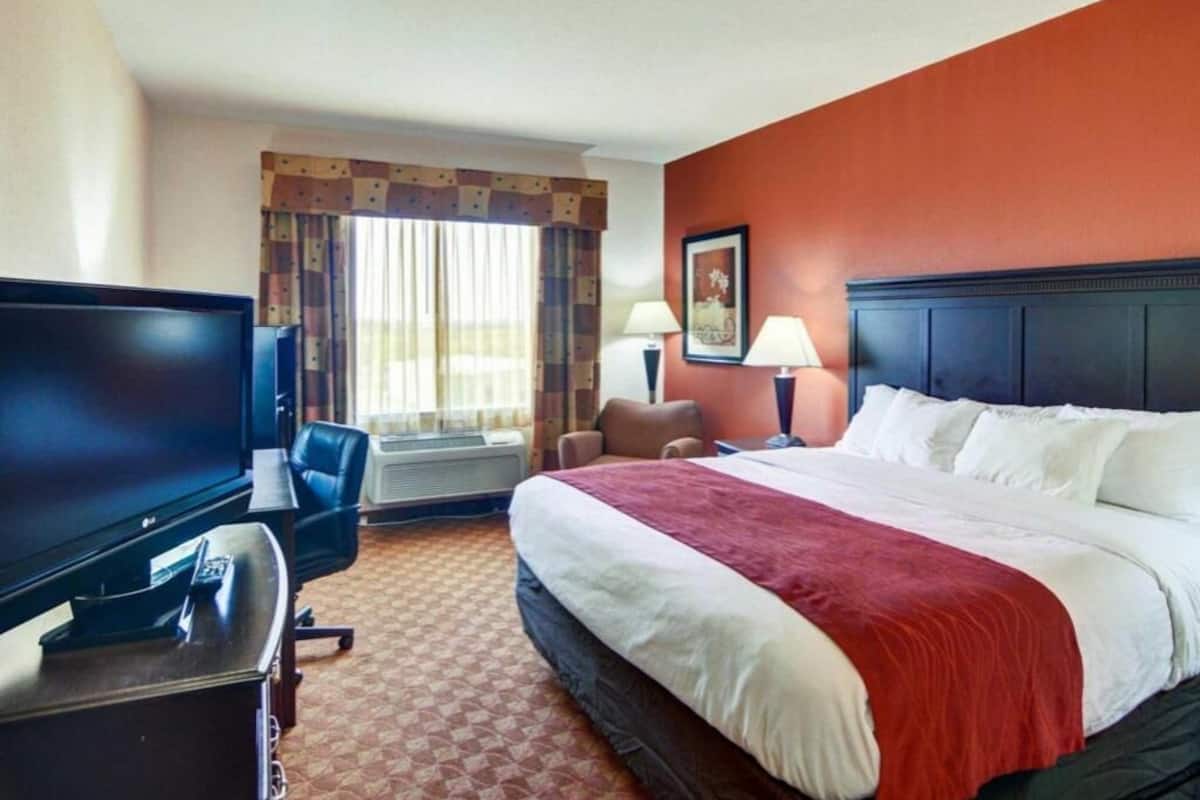 A hotel room with a bed, a television, a desk, a chair, and a window with curtains.